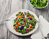 Blick von oben auf einen leckeren Salat mit Linsen und Gemüse, garniert mit Walnüssen, serviert auf einem weißen Teller neben einer Schale mit Basilikumblättern