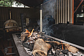 Heißes brennendes Holz in einem schwarzen Kohlenbecken mit Flammen und Kohle neben einem modernen Grill auf der Terrasse eines Cafés mit Mauern