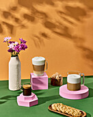 Composition of glass cups with aromatic coffee placed against raisin cookies and vase with flowers on green table