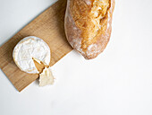 Von oben köstlicher Camembert-Käse auf einem hölzernen Schneidebrett neben Brot auf weißem Hintergrund