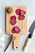 Top view composition of ripe raw beetroot slices placed on wooden cutting board on kitchen table near sharp knife