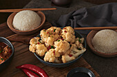 Close up cauliflower dish, accompanied by a bowl of rice, soy sauce and a Japanese teapot on top of a wooden table decorated with fabrics