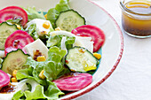 Leckerer vegetarischer Salat mit Gurke und Roter Bete mit grünen Blättern und Eiern mit Mais und Soße in einer Schüssel auf dem Tisch neben Geschirr mit Honig