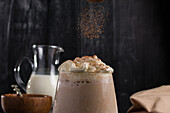 Closeup of falling aromatic ground cinnamon on top of milkshake with ice vanilla and whipped cream in glass