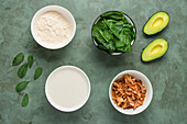 Top view of ingredients for keto diet green smoothie preparing with protein powder with spinach and avocado mixing with milk in blender and with adding toasted coconut chips