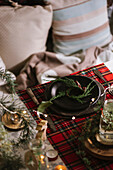 From above Christmas table setting with wreath on ceramic plate on red checkered tablecloth on the background