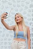Blonde female with blond hair taking self shot on mobile phone in city street