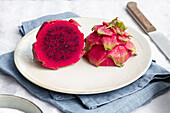 Leuchtend leckere Pitaya mit saftigem Fruchtfleisch und kleinen Kernen auf Keramikteller neben Messer auf Tisch