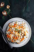 Overhead view of tasty cake with cream cheese and crunchy nuts with fresh carrot slices on top