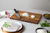 Von oben Holzbrett mit geschnittener Zwiebel und Messer neben Erbsen und Seehechtfilet mit Kräutern bei der Zubereitung von Speisen in der Küche