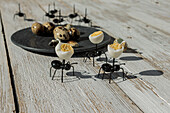 From above of toy black ants placed near plate with quail eggs on wooden table in sunlight