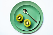 From above of halved fresh yummy kiwi and silver spoon placed on green ceramic plates on white background