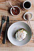 Appetitliche Scheibe Körnerbrot mit Avocado und pochiertem Ei auf einem Teller auf einem Holztisch