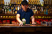 Young Asian bartender gives you a grapefruit juice gin cocktail in the bar after he finished to prepare it