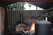 Hot burning wood in black brazier with flames and coal placed near modern barbecue grill on terrace of cafe with walls