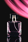 Composition of stylish perfume bottle with lid placed on black background near pink luminous illumination