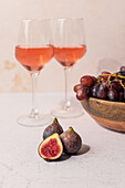 Glasses of red drink placed on table with bowl of grapes and figs