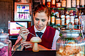 Fröhliche Barkeeperin dekoriert einen sauren Cocktail in einem pilzförmigen Glas auf dem Tresen einer Bar