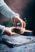Hand of crop unrecognizable person catching chickpeas into bowl on table with towel and green plants in light kitchen