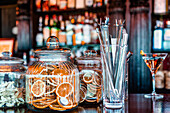 Bartender metal tools in glass and assorted decorations in jars placed on wooden counter in pub