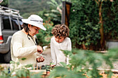 Gärtnerin, die Samen aus einer Plastiktüte nimmt, um sie in einem Gartenbeet mit einem kleinen Sohn auf dem Land zu pflanzen