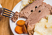 Leckeres hausgemachtes Corned Meat mit Kohlstücken und Karotten auf einem Teller auf einem Holztisch serviert