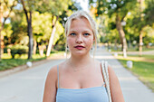 Frau mit blondem Haar steht an einem sonnigen Tag im Sommerpark und schaut in die Kamera