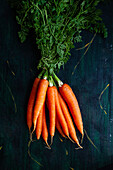 Top view of bunch of whole raw carrots with stems and leaves on wooden surface
