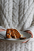 Crop anonymous cook holding plate with tasty carrot cake slice with cream cheese and moist biscuit