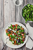 Blick von oben auf einen leckeren Salat mit Linsen und Gemüse, garniert mit Walnüssen, serviert auf einem weißen Teller neben einer Schale mit Basilikumblättern