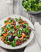 Top view of tasty salad with lentils and vegetables topped with walnuts served on white plate near bowl of basil leaves