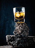 Whiskey mit Eiswürfeln, serviert in einem Kristallglas auf einer rauen Oberfläche vor schwarzem Hintergrund
