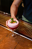 Hände eines nicht erkennbaren Barkeepers, der einen Cocktail mit Minzblättern und Passionsfrucht in einer Bar serviert