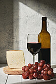 Arrangement aus aromatischem Rotwein im Glas, serviert auf dem Tisch neben Weinflasche, reifen Trauben und dreieckigem Käsestück