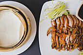 From above composition of sliced Beijing duck on white ceramic plate with traditional bamboo steamers