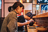 Side view of woman and man communicating while eating Asian food at wooden counter in modern cafe