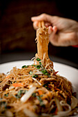 Hands with chopsticks pulling noodles from plate with beef vegetable noodles portion