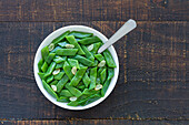 Blick von oben auf gesunden Salat mit grünen Bohnen und Knoblauchscheiben in einer Schüssel auf einem Holztisch