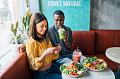 Vloggerin mit schwarzem Partner fotografiert in einem Restaurant mit dem Handy eine gesunde Mahlzeit von oben