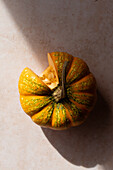 Top view of fresh rip pumpkin with cut piece placed on beige marble table on sunny day in kitchen