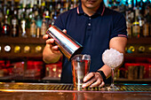 Hands of unrecognizable bartender holding a shaker for mixing a cocktail in the bar