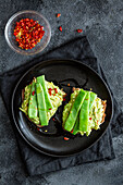 Appetitliche Toasts mit frischer Guacamole und grünen Erbsenschoten, garniert mit rotem Paprika und serviert auf einem schwarzen Teller