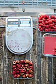 Top view of ripe sweet raspberries in plastic containers placed near digital scales for measuring weight