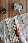 Top view of anonymous person slicing thin dough on wooden table near cream cheese and fig jam during pastry preparation