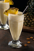 Süßer, erfrischender, kalter Pina-Colada-Smoothie, serviert mit Ananasscheiben auf einem Tisch mit gestreuten Mandeln