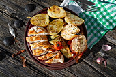 Tasty grilled chicken breast served on plate with fresh roasted cherry tomatoes and zucchini placed on wooden table with onion