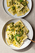 Top view of appetizing cooked ravioli pasta with green sauce and herbs placed on white plates with fork on table