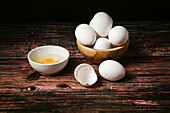 Uncooked eggs in bowl placed on wooden table in dark background for cooking breakfast