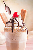 Spoon reaching to appetizing sweet milkshake decorated with whipped cream and waffles and cherry on top