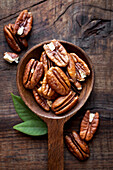 From above shelled Pecan nuts in a wooden spoon bowl against dark rustic background